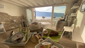 A dining area with a view of the sea, a stone wall, and a wooden table with food items and containers. - Vista Lago (Toscolano Maderno)