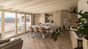 A spacious dining area with a large table and chairs, a stone wall, and a view through glass doors to the outside. - Vista Lago (Toscolano Maderno)