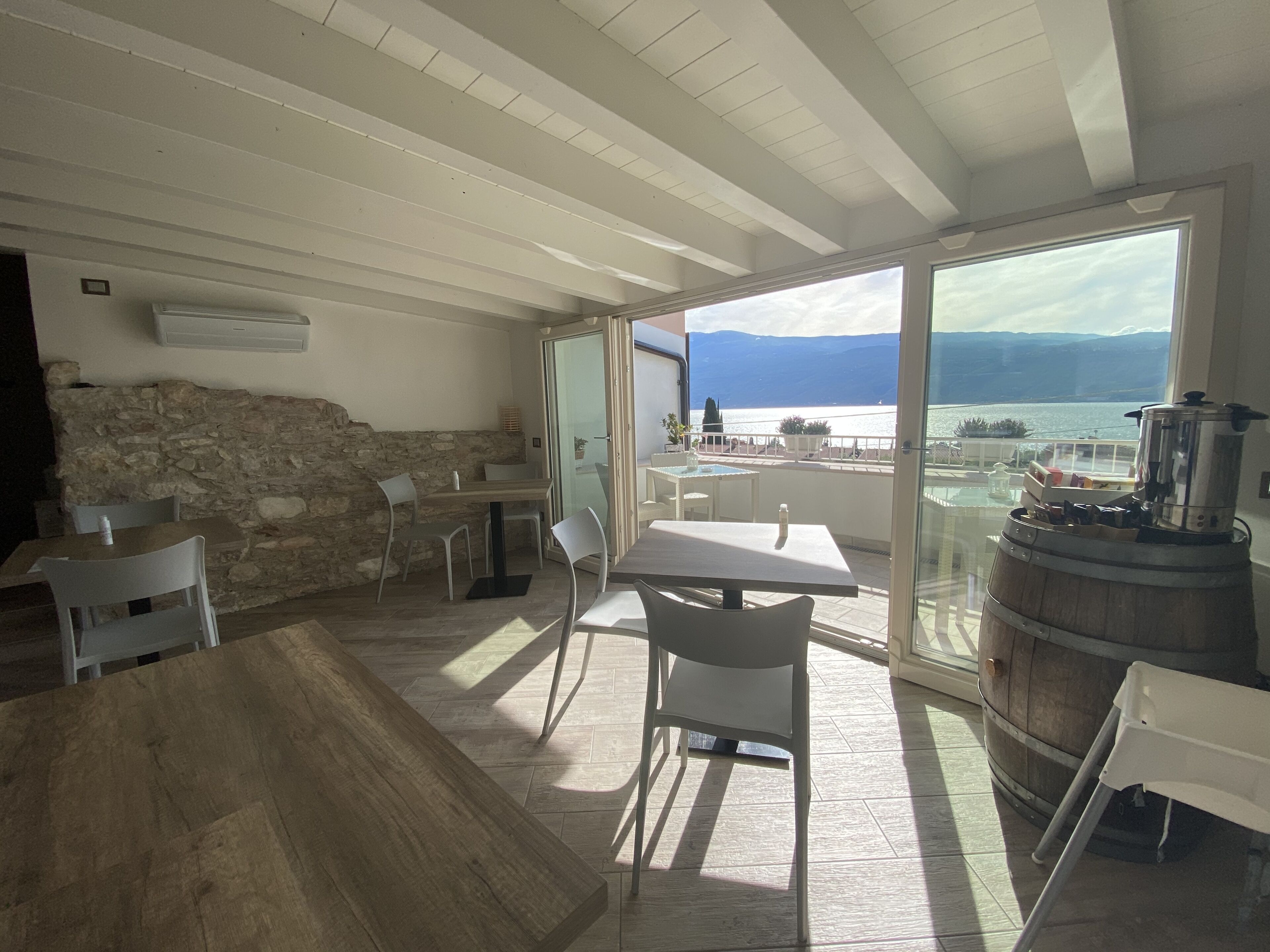 Ein Essbereich mit Steinwand, Holztisch und Stühlen. Durch große Fenster ist Meer und Berge zu sehen.