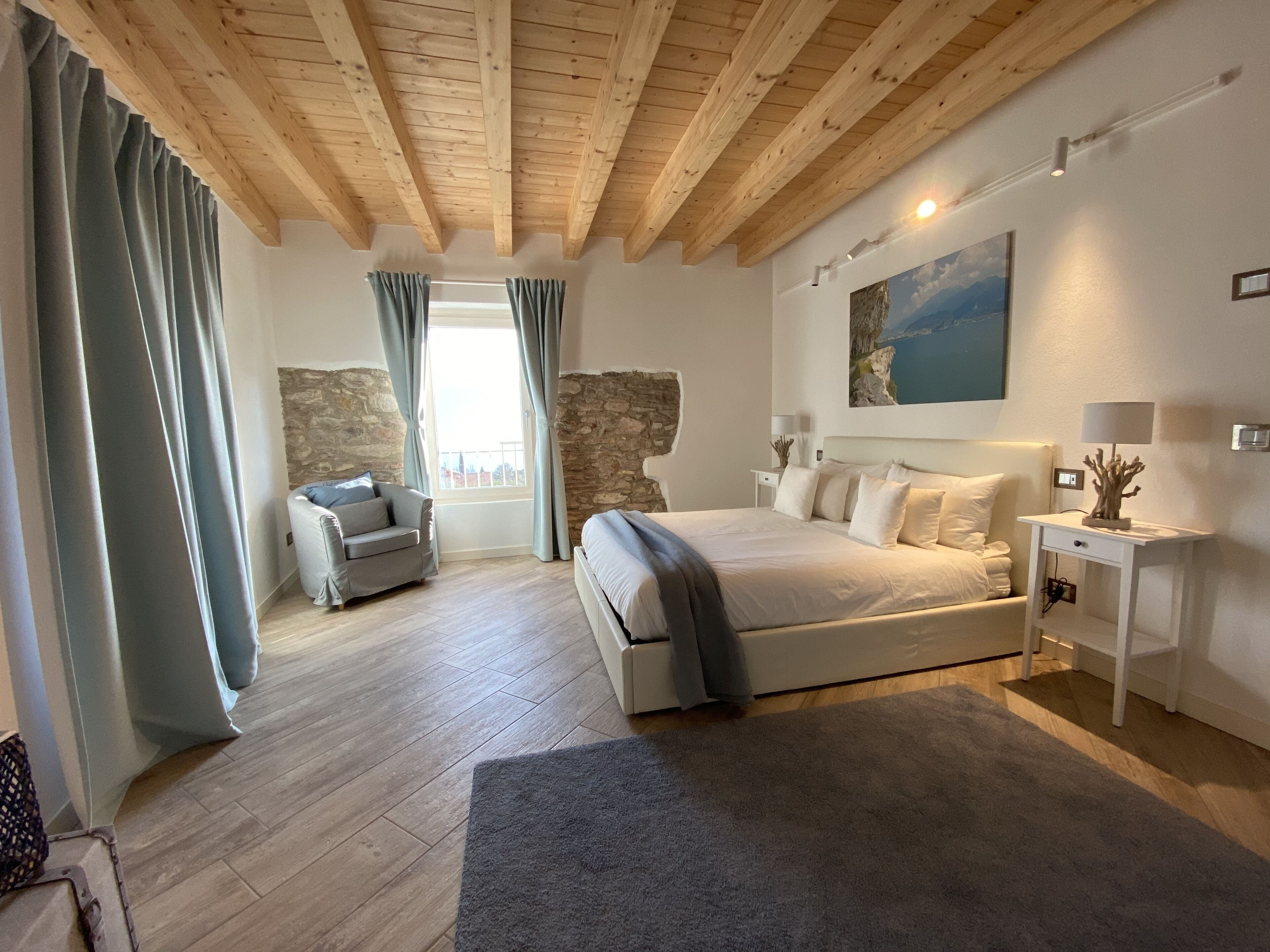 Un dormitorio con una cama grande, una silla, una mesita de noche y una pared de piedra.