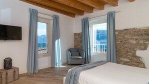 A bedroom with a bed, a TV, a stone wall, and a view of the sea. - Vista Lago (Toscolano Maderno)