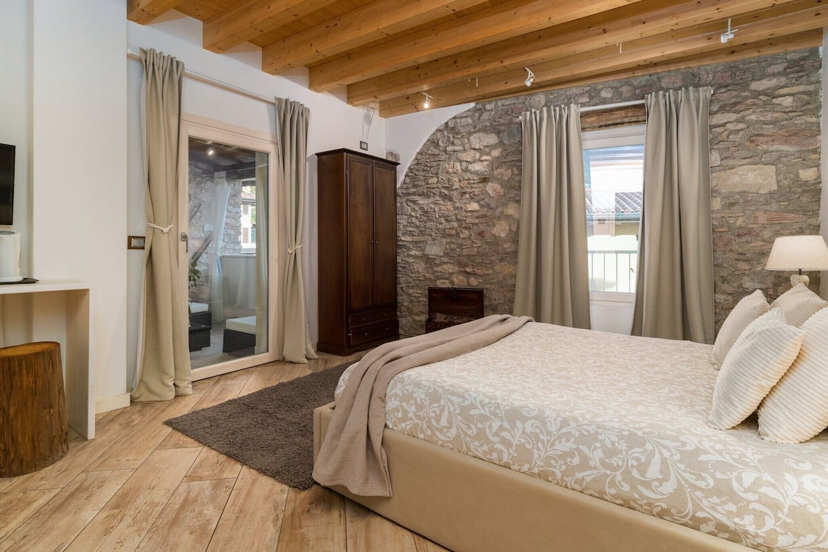 A bedroom with a stone wall, wooden ceiling, and a bed with patterned bedding.