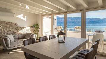 Ein geräumiger Essbereich mit großem Tisch und Stühlen, einer Steinsäule und Blick auf das Meer und die Berge durch große Fenster.