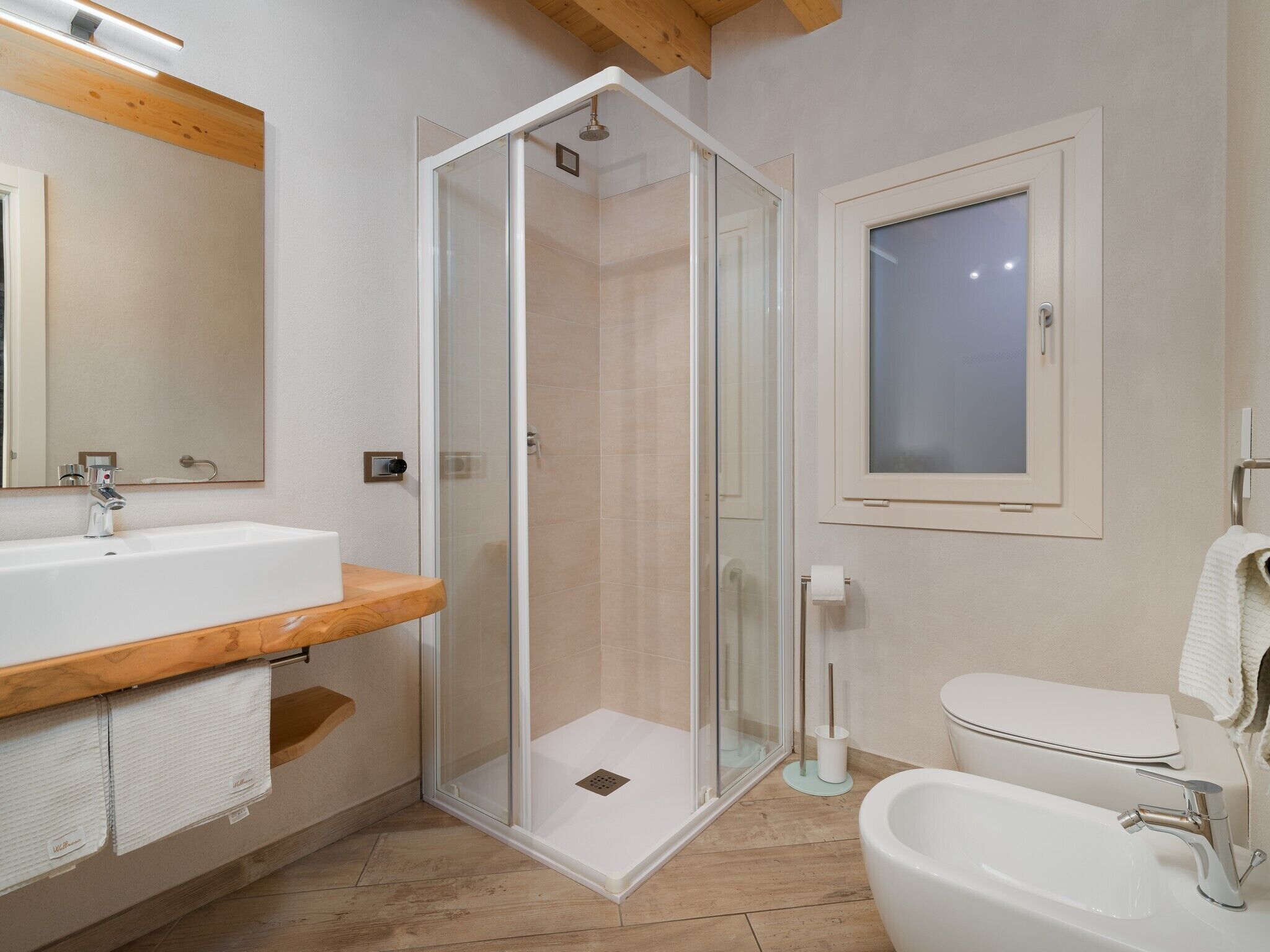 A modern bathroom with a glass-enclosed shower, a sink with a wooden countertop, a toilet, and a mirror.