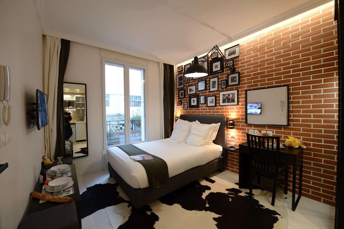 A modern hotel room with a brick wall, a large bed, a desk, and a television.
