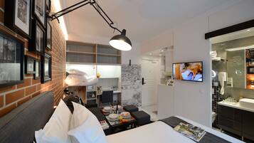 A hotel room with a bed, a desk with a chair, a TV, and a bathroom with a mirror and sink.
