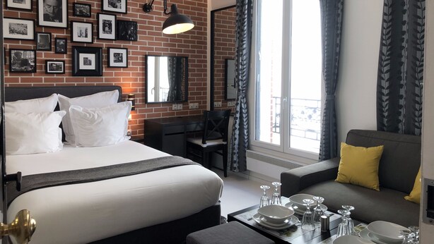Habitación de hotel con pared de ladrillo, cama, escritorio, sofá y una mesa de comedor con platos y vasos.