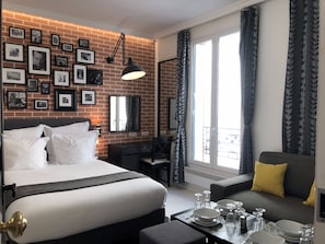 Ein Hotelzimmer mit Backsteinwand, einem Bett, einem Schreibtisch, einer Couch und einem Esstisch mit Tellern und Gläsern.