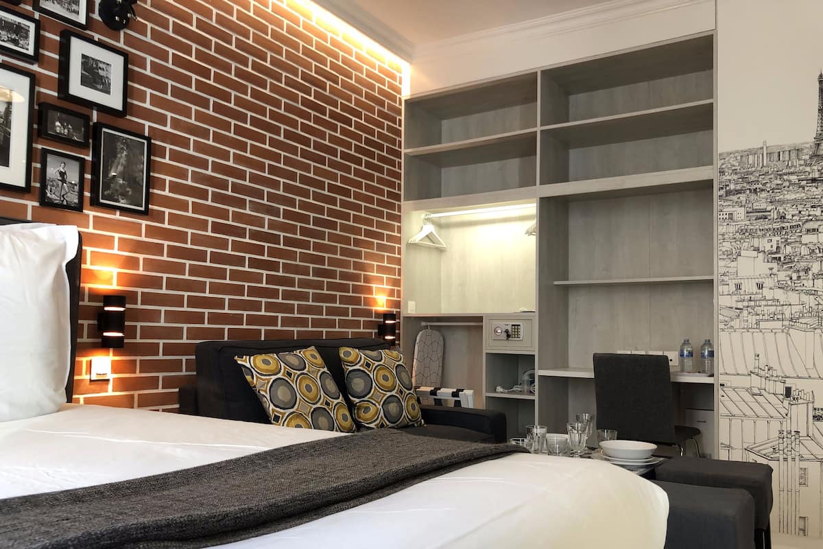A hotel room with a brick wall, a bed with patterned pillows, a wardrobe with shelves, and a map mural on the wall.