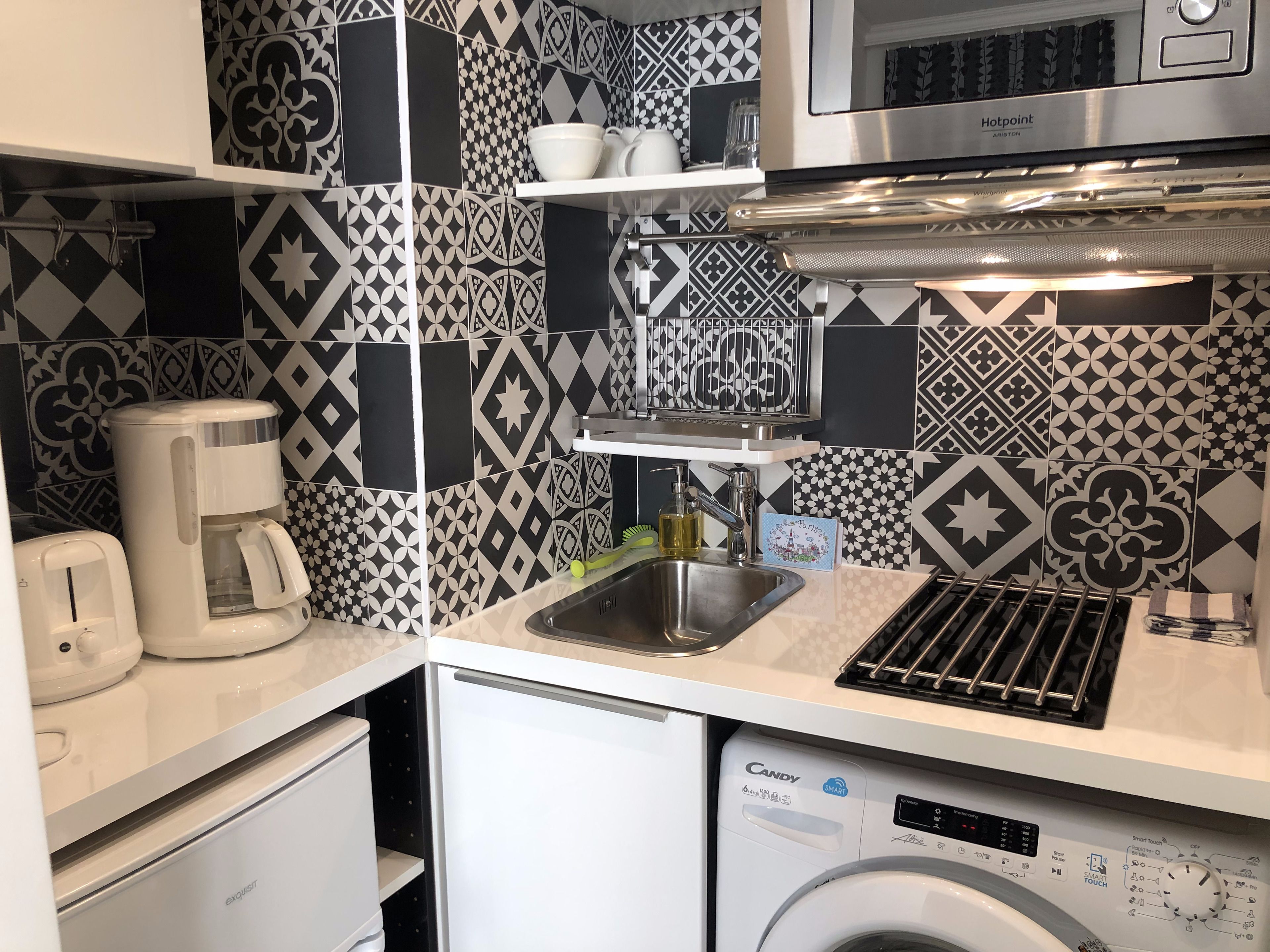 A compact kitchen with a coffee maker, a microwave, a sink, and a washing machine.
