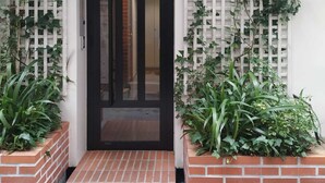 Una entrada frontal con una puerta negra, paneles de celosía blanca y plantas en macetas.