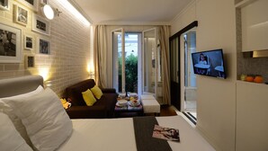 Habitación de hotel con una cama, un sofá, una mesa de comedor con platos y vasos, un televisor en la pared y un balcón con cortinas.