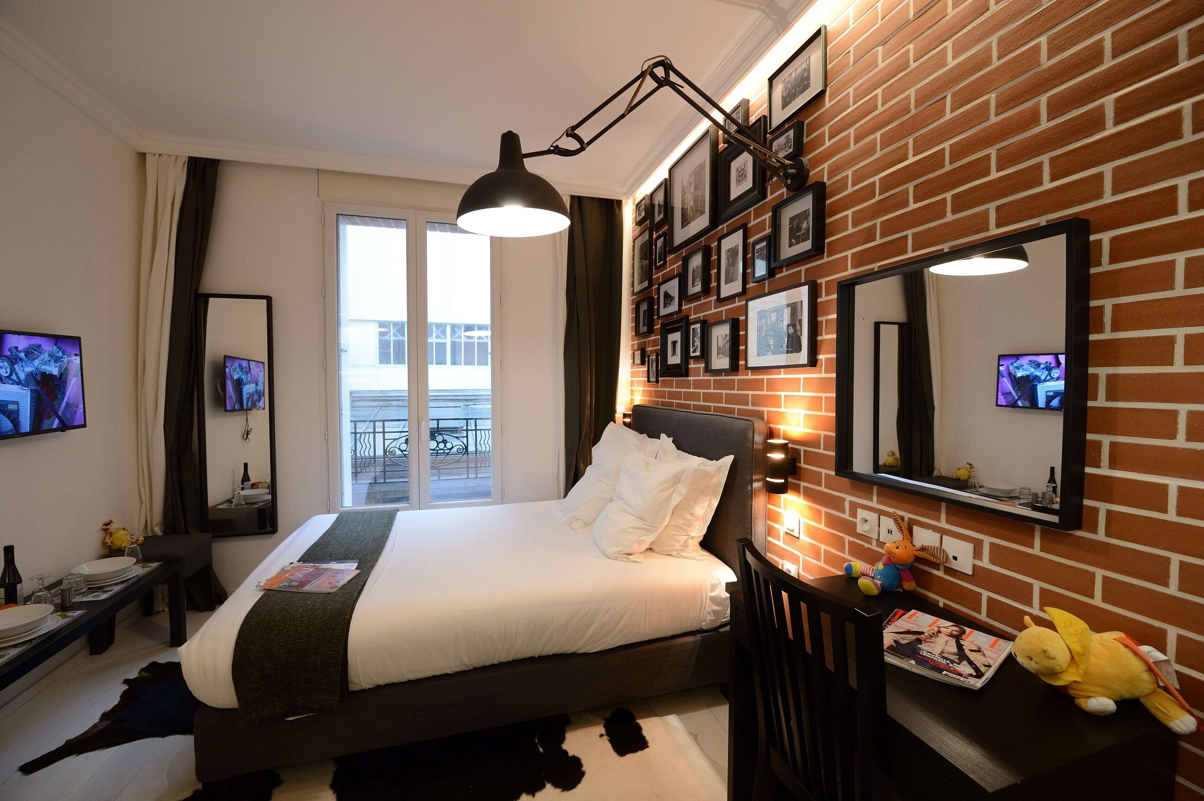 A hotel room with a brick wall, a large bed, a desk with a chair, a TV, and a balcony view.