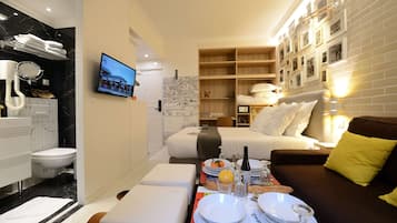 Een moderne hotelkamer met een zithoek, een bed met wit beddengoed, een bruine bank met een geel kussen en een wand met ingelijste foto's.