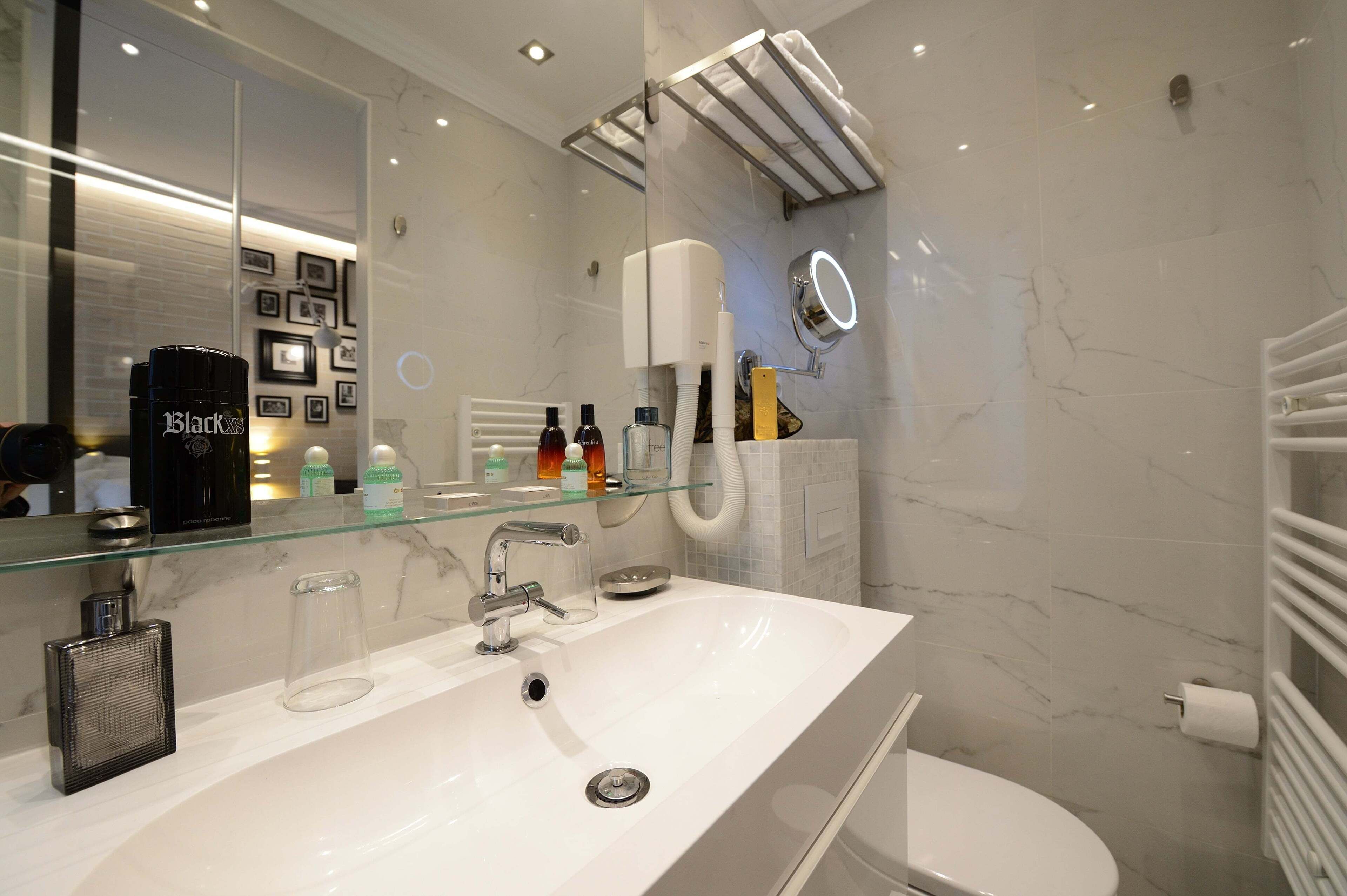 Un baño moderno con un espejo grande, un lavamanos blanco y una mampara de cristal para la ducha.