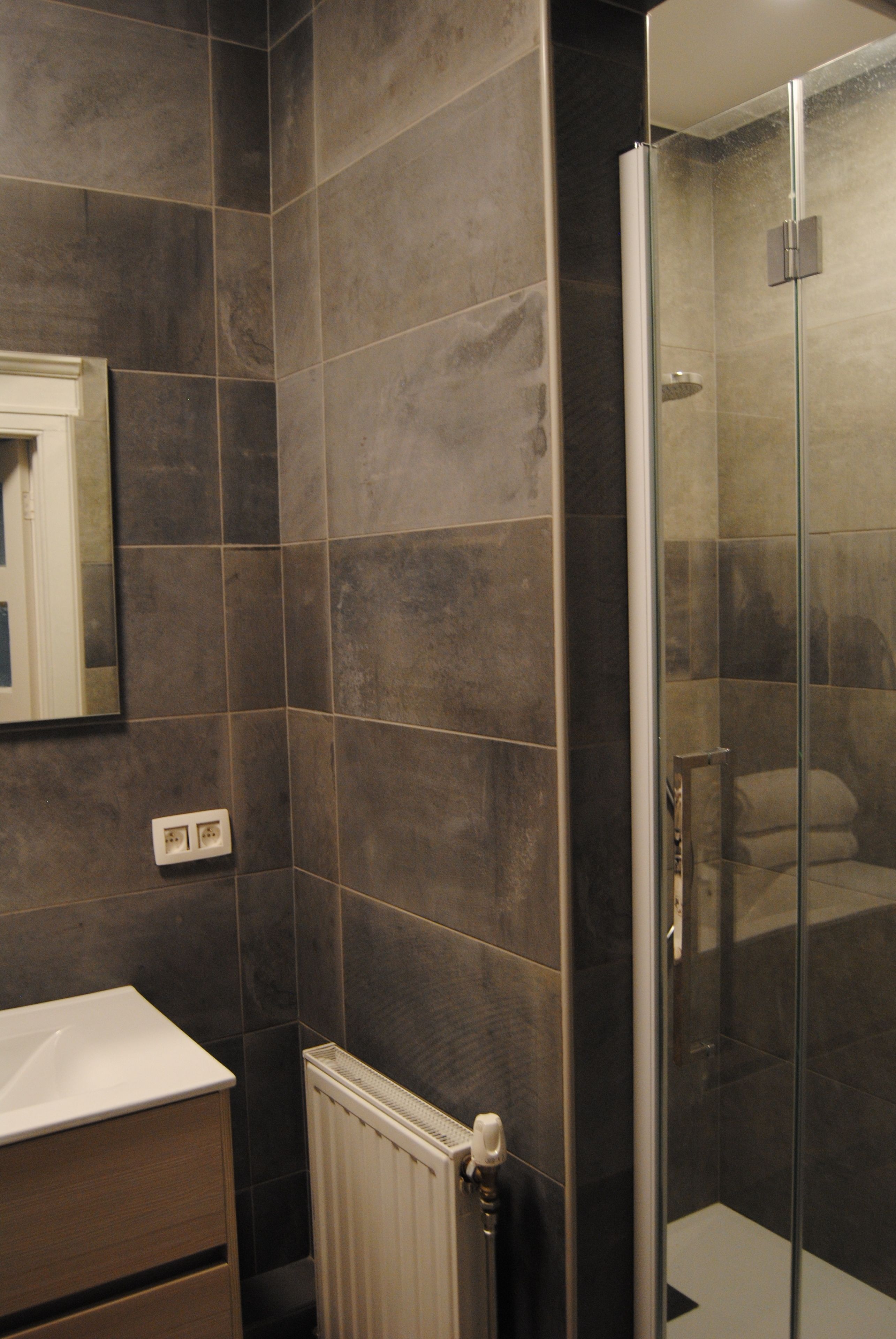 A bathroom with dark tiles, a glass shower enclosure, and a white sink.