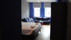 A hotel room with a bed, two sofas, a small table, and a window with a view of buildings. - L'Inattendu sur la Croisette Dinant Centre (Dinant)