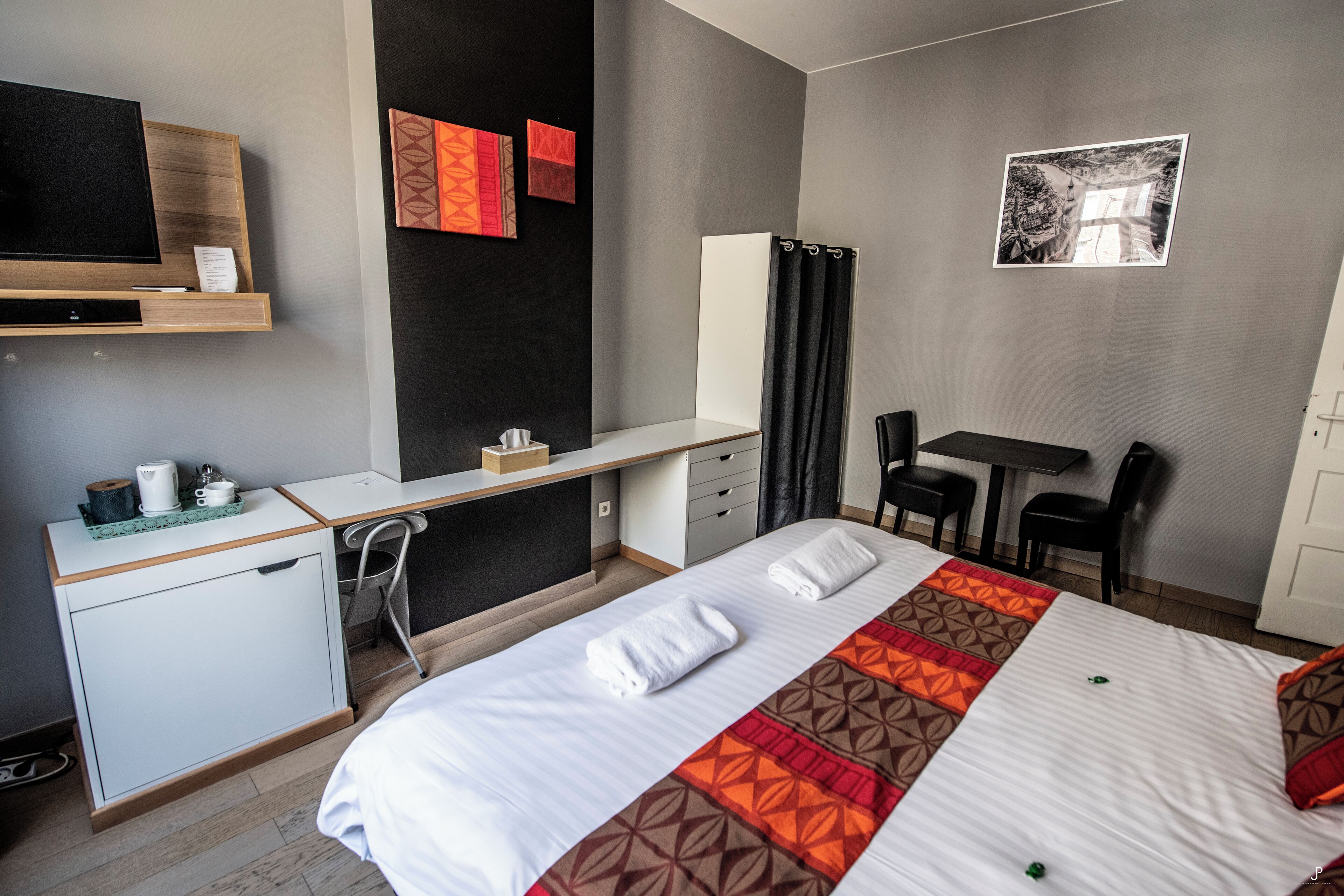 Una habitación de hotel con cama, escritorio, silla, televisor y obras de arte en las paredes.