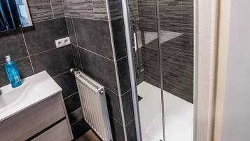 Une salle de bain moderne avec une douche à parois de verre, des carreaux foncés, un lavabo blanc et un miroir.