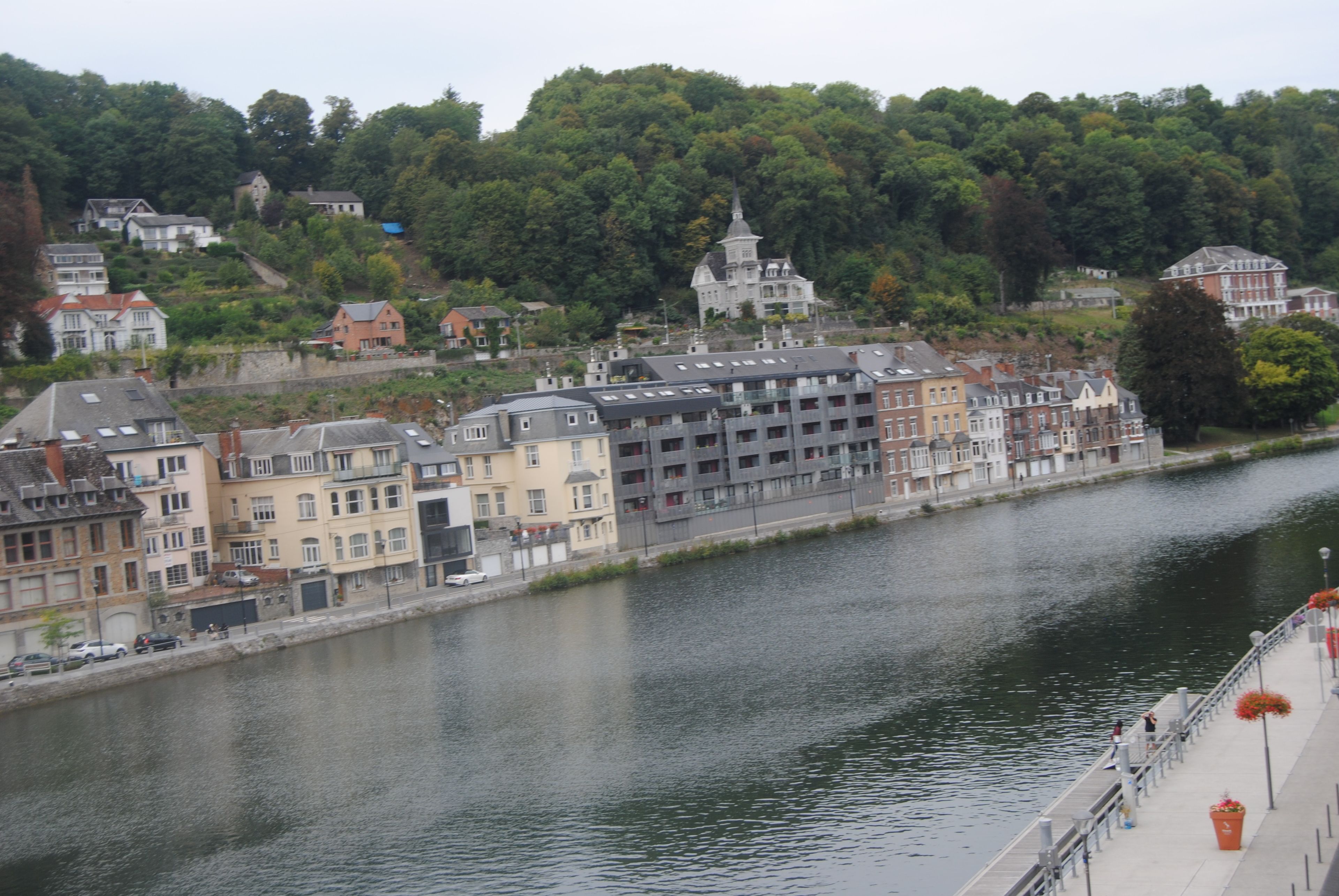 A riverside view of a town with historic buildings, a prominent church, and a bridge.