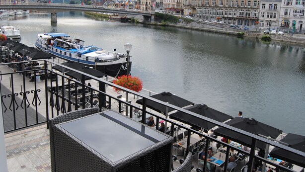 A riverside restaurant with outdoor seating overlooking a river, a bridge, and historic buildings in the background. - L'Inattendu sur la Croisette Dinant Centre (Dinant)