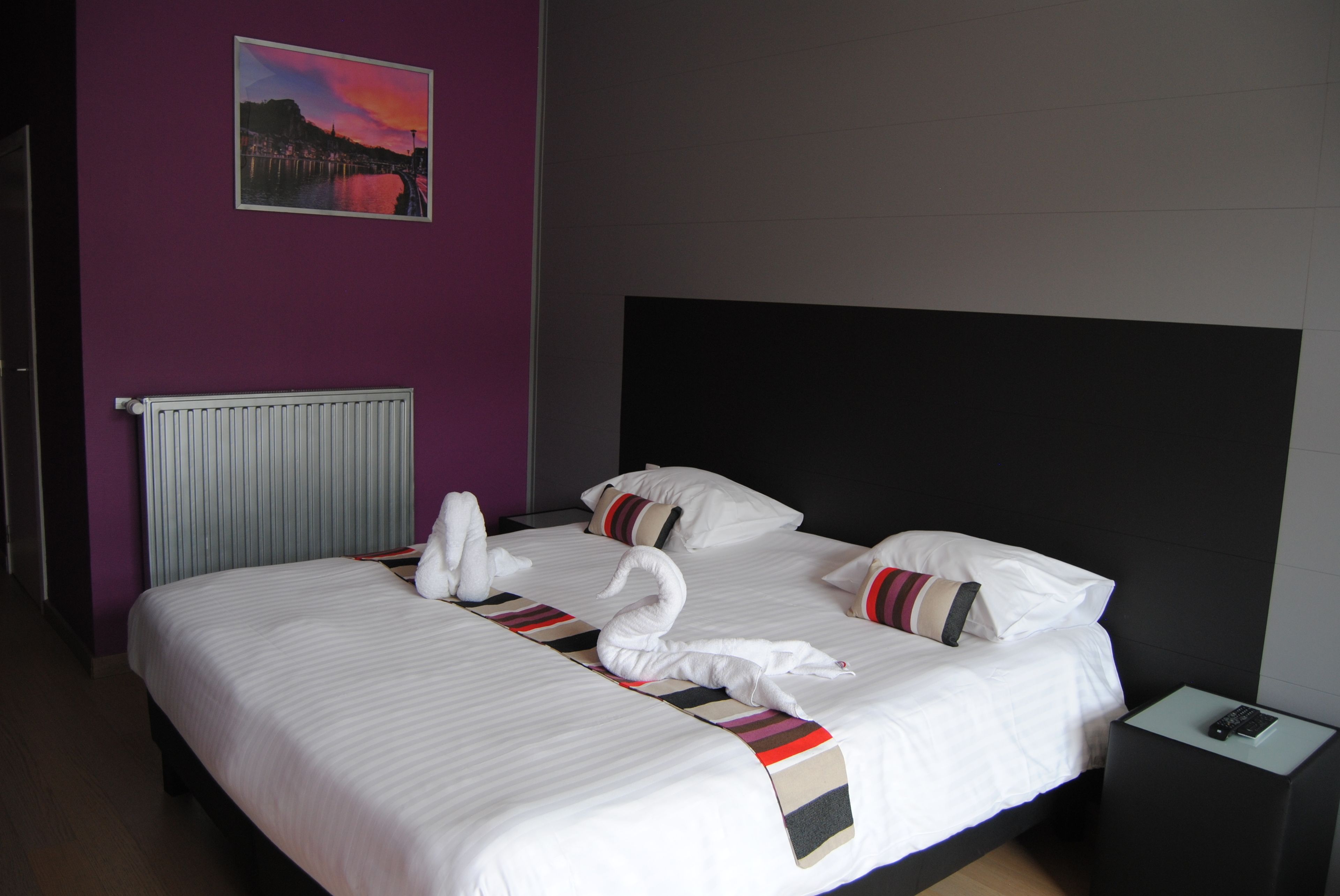 Et hotelværelse med en stor seng, sengegavl, et natbord, et billede på væggen og en radiator.