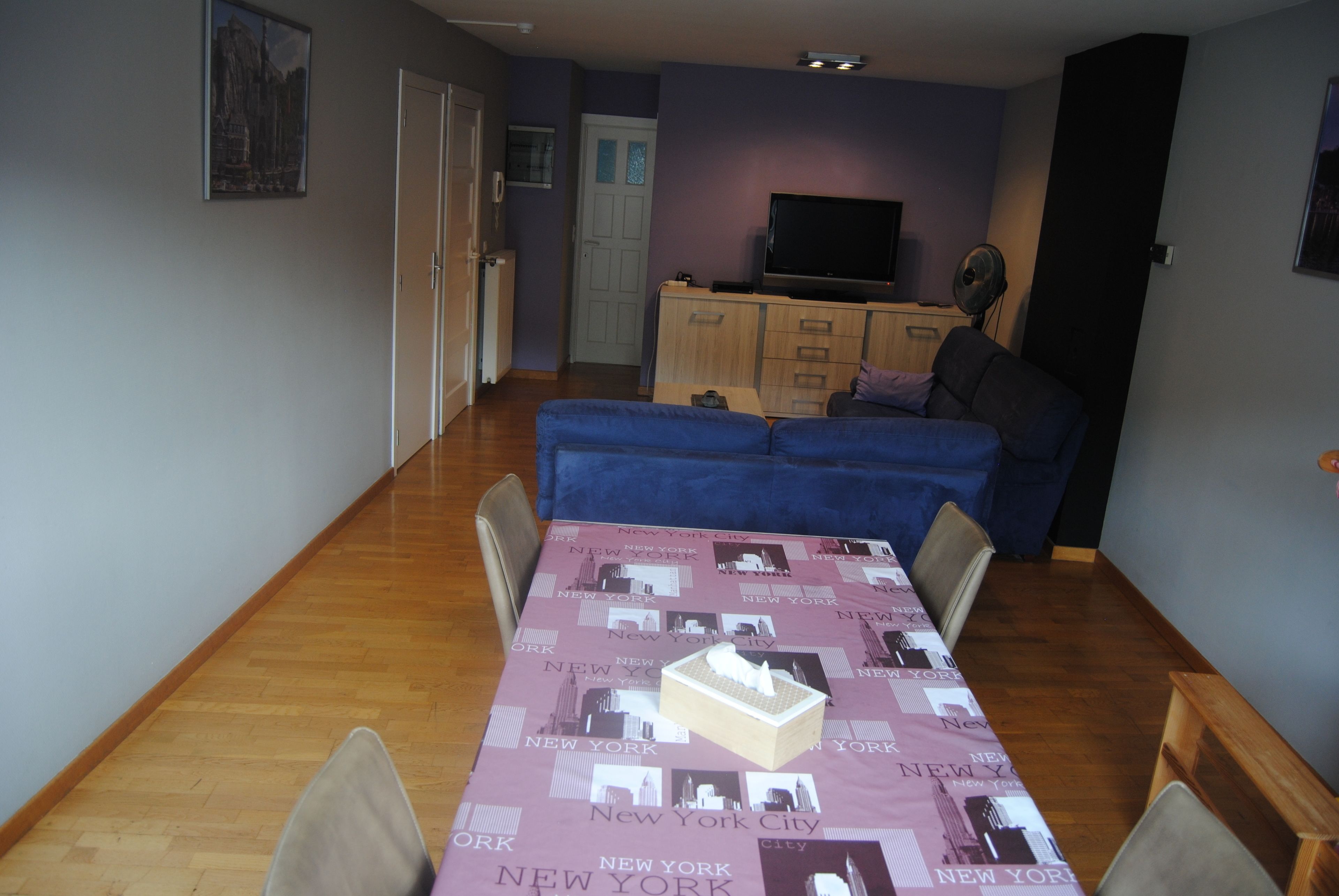 Een zithoek met een tafel bedekt met een tafelkleed met New York City-thema, een bank en een televisie op de achtergrond.