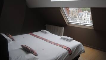 Une chambre d’hôtel avec un grand lit, une lucarne et une vue sur les bâtiments environnants.