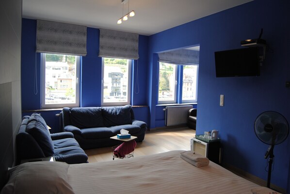 A room with a bed, a sofa, a small table with a box, and a standing fan. - L'Inattendu sur la Croisette Dinant Centre (Dinant)