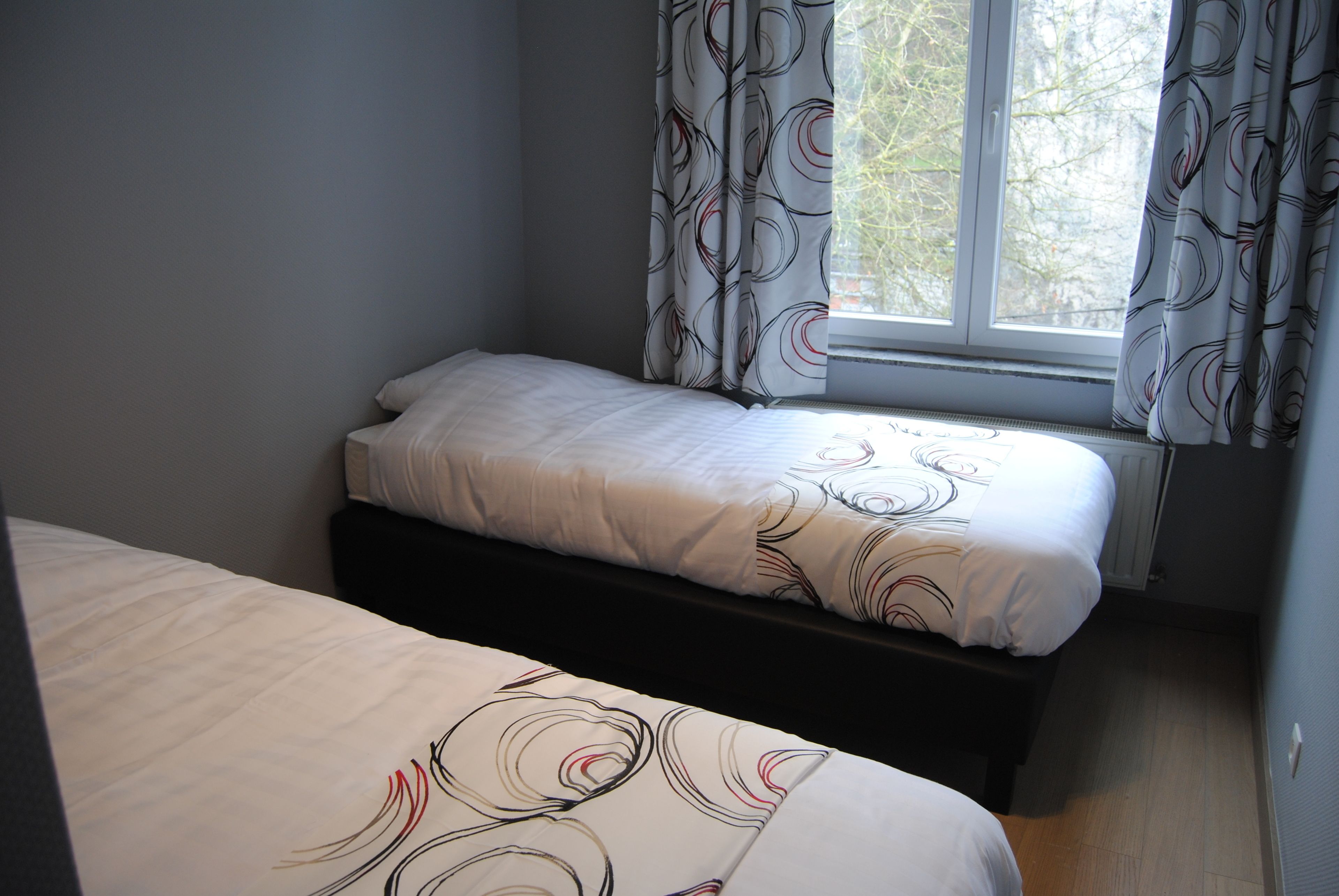 A bedroom with two single beds, a window with curtains, and a radiator.