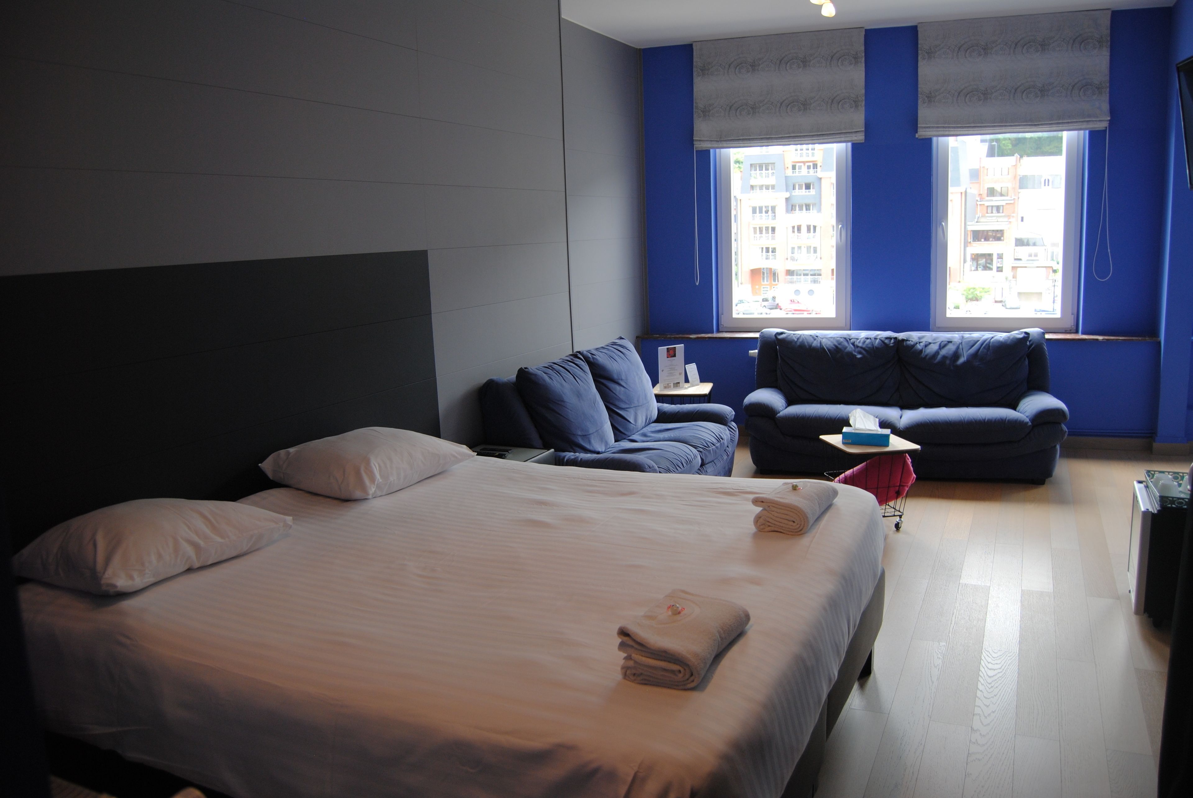Una habitación de hotel con una cama grande, dos sillones, una mesita y una ventana con vista a la ciudad.