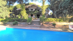 A poolside view of a house with a swimming pool, surrounded by greenery and a stone staircase leading to the entrance. - Casa Rural Viña Arroyo del Galloo (Andújar)