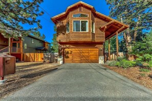 A two-story wooden cabin with a garage, surrounded by trees.
