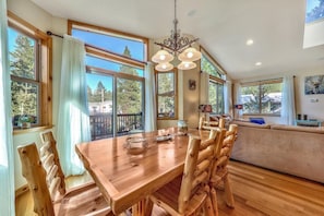 A spacious dining area with a wooden table and chairs, large windows offering views of the outdoors, and a chandelier hanging above. - Come play in the mountains: Lake, explore and relaz. (South Lake Tahoe)