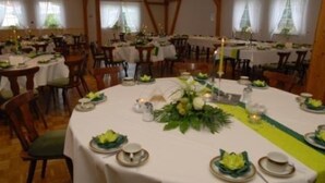 Un espace repas avec des tables rondes dressées pour le service, agrémenté de nappes blanches, de serviettes vertes et de centres de table floraux.