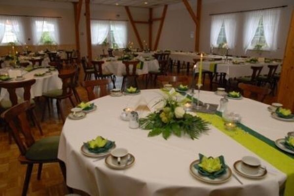 Ein Essbereich mit runden Tischen, gedeckt für eine Mahlzeit, mit weißen Tischdecken, grünen Servietten und floralen Mittelstücken.
