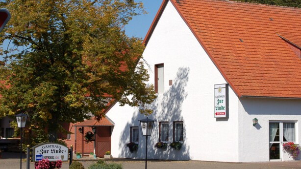 Un bâtiment blanc avec un toit rouge, une enseigne indiquant « Gasthaus Zur Linde » et une autre indiquant « Gasthof ».