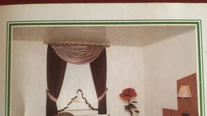 Une chambre avec un lit simple, une chaise, une table de chevet, une lampe et une fenêtre avec des rideaux.