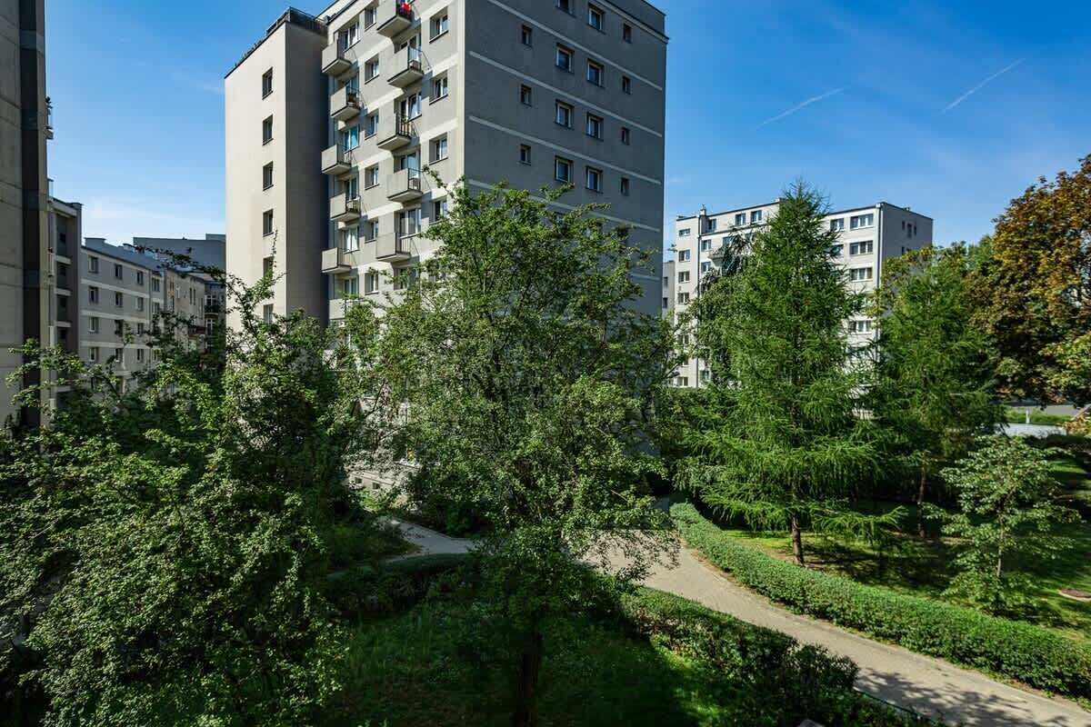 Un immeuble résidentiel à plusieurs étages, doté de balcons, entouré d’une végétation luxuriante et surplombant un ciel dégagé.