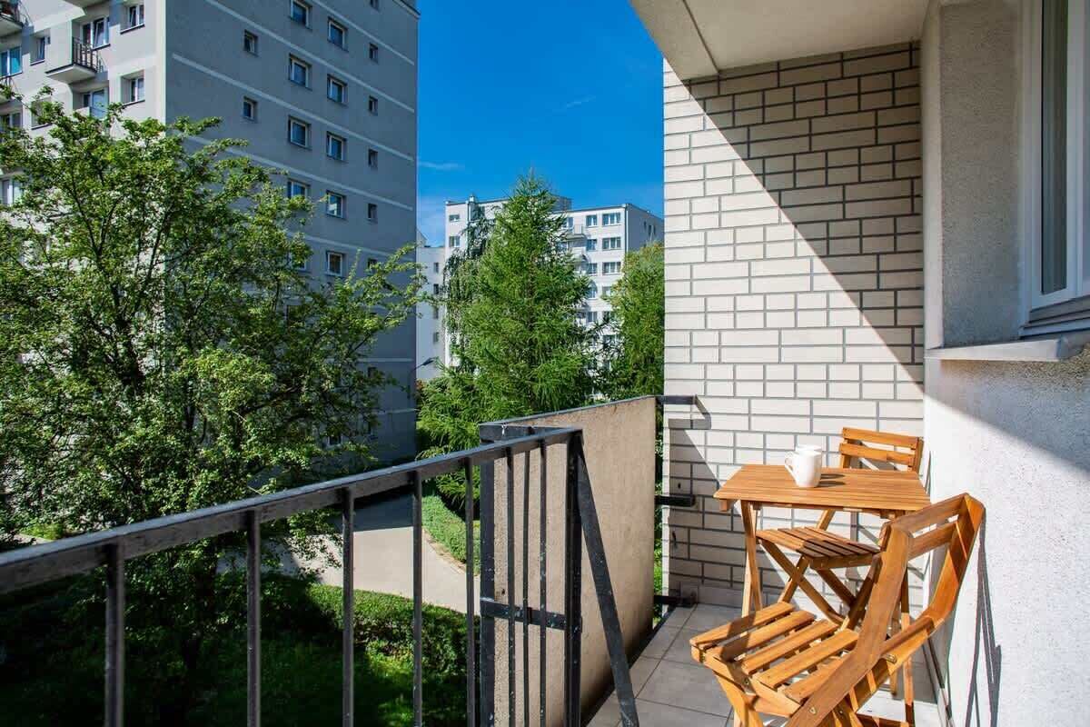 Un balcon avec une table et des chaises, une vue sur les immeubles voisins et un mur en briques.