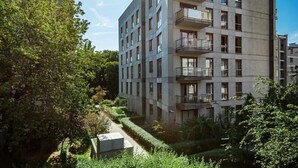 A modern multi-story residential building with balconies, surrounded by lush greenery and a well-maintained garden.