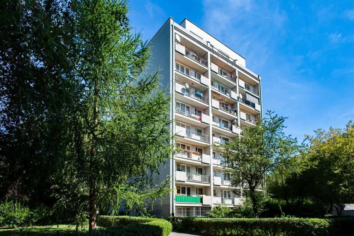 Een meerlaags woongebouw met balkons, omringd door groen en bomen.