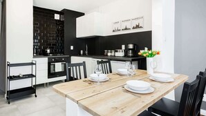 A modern kitchen with black and white cabinetry, a wooden dining table set for four, and a cityscape wall art above the counter.