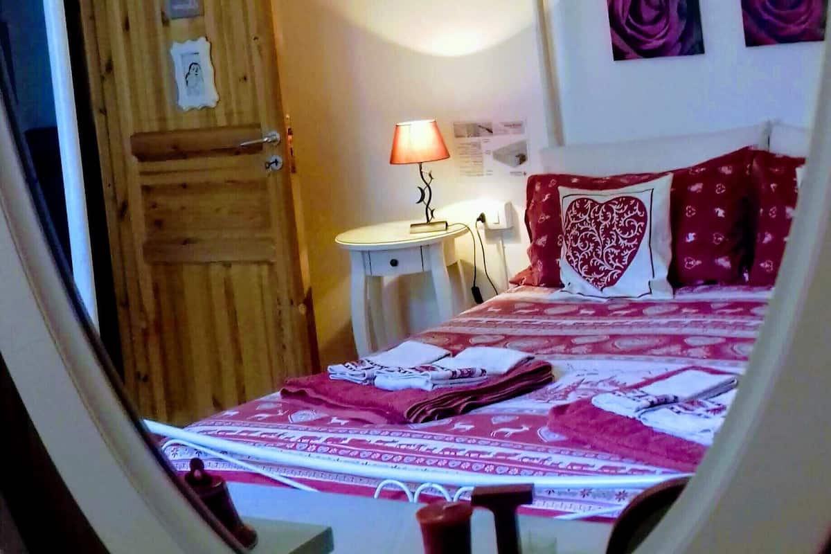 A bedroom with a four-poster bed, a bedside table with a lamp, and a wooden door.