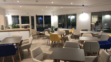 Un espace repas moderne, doté de tables et de chaises, de grandes fenêtres et de plantes d’intérieur.