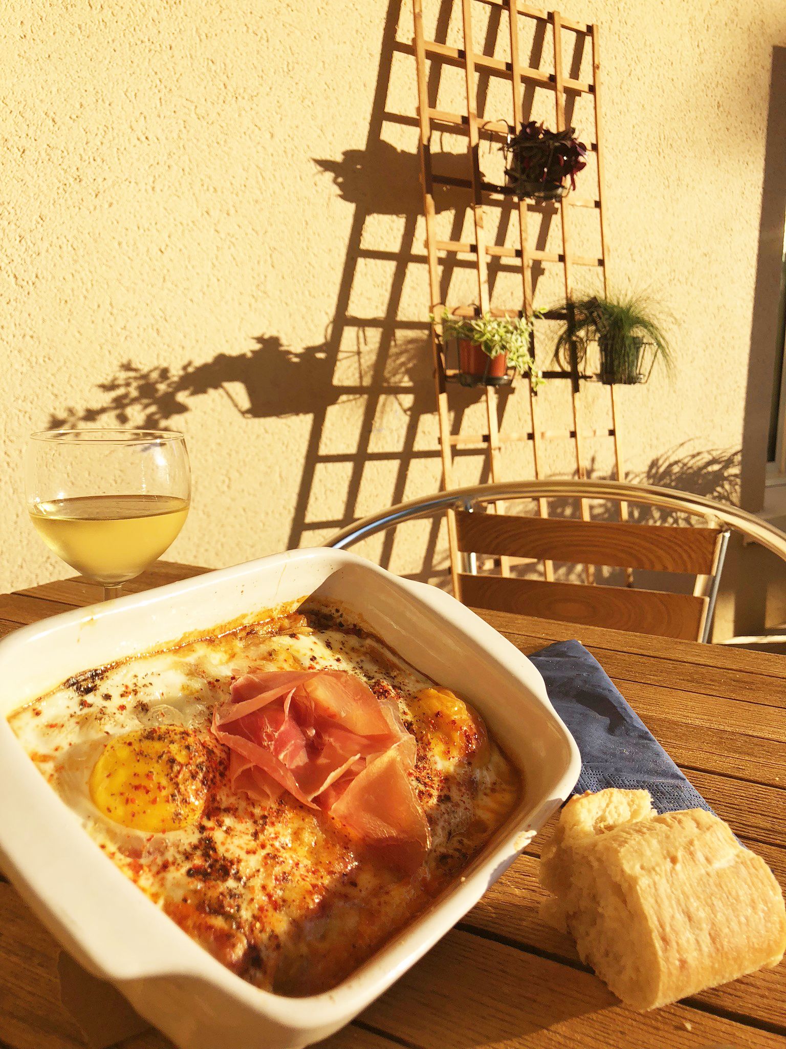 Ein Teller mit Eiern, Schinken und Käse auf einem Tisch, an dem ein Holzhocker und ein Weinglas stehen.