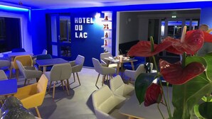 A modern hotel lobby with blue lighting, a 'HOTEL DU LAC' sign, and a variety of seating arrangements including tables and chairs. - Hotel du Lac d'Arjuzanx (Morcenx-la-Nouvelle)