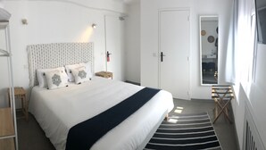 A bedroom with a bed, a bedside table, a hanging wardrobe, a small stool, and a window with curtains. - Hotel du Lac d'Arjuzanx (Morcenx-la-Nouvelle)