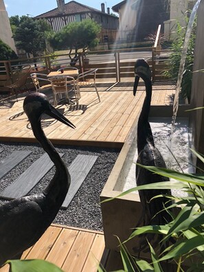 A wooden deck with two large bird sculptures, a small water feature, and a seating area with chairs and tables. - Hotel du Lac d'Arjuzanx (Morcenx-la-Nouvelle)