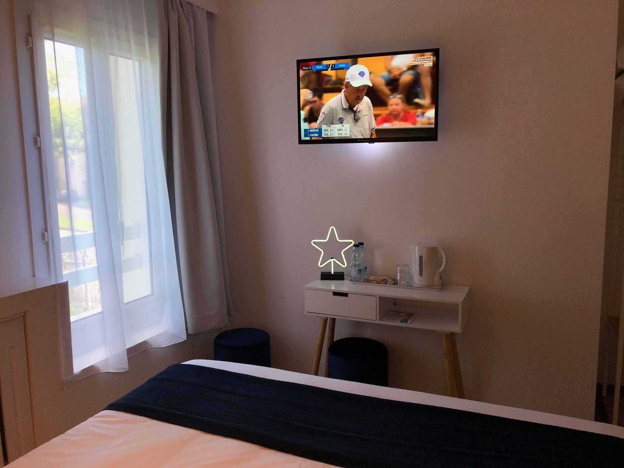 A hotel room with a bed, a desk with a star-shaped light, a television displaying a golf tournament, and a window with curtains.